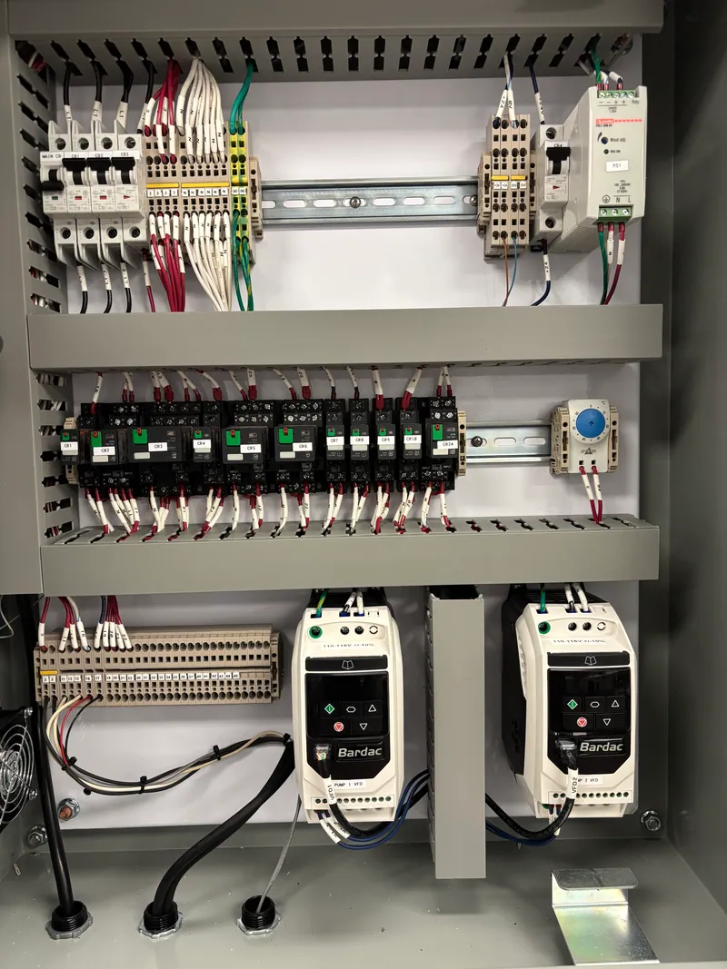 Inside a duplex pump control panel: breakers and labeled terminal blocks along the top, a row of control relays, and two Bardac variable frequency drives, one per pump