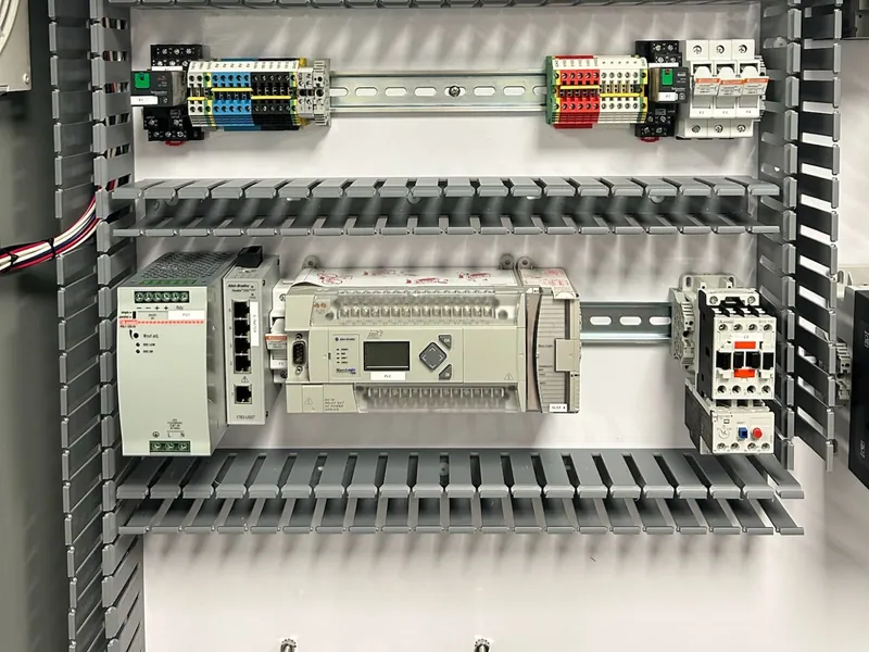 An Allen-Bradley PLC on a DIN rail beside a network switch, a power supply and a motor contactor, with terminal blocks, relays and fuses on the rail above