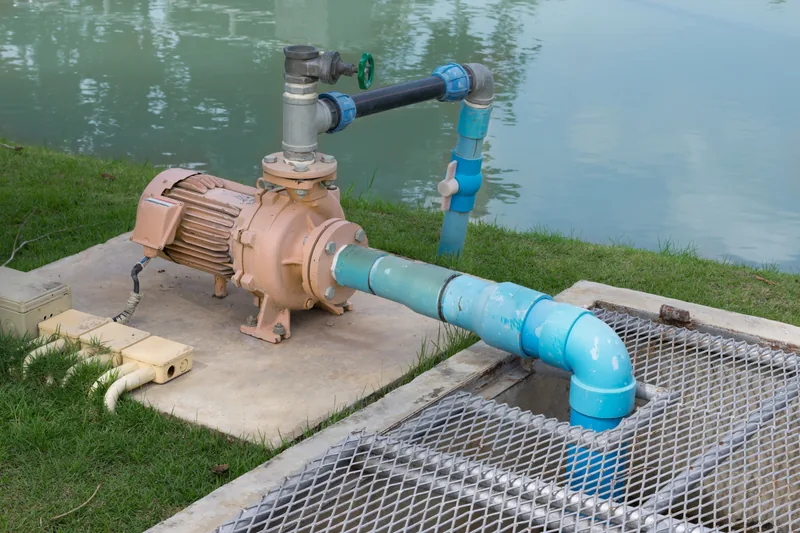 An electric water pump and pipework at the edge of a lake